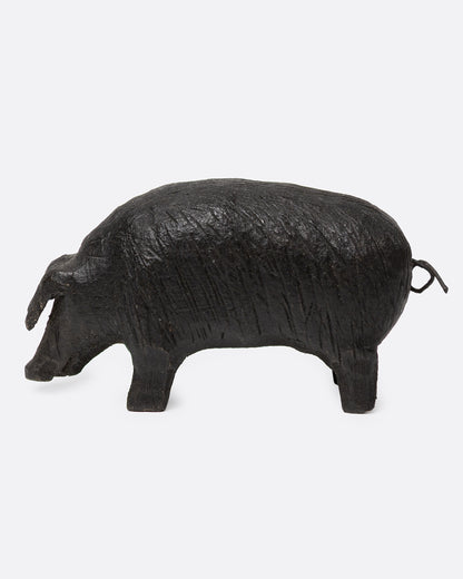 A wooden hand carved pig figurine with a wire tail, shown from the side.