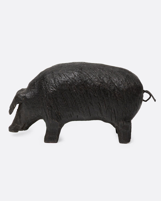 A wooden hand carved pig figurine with a wire tail, shown from the side.