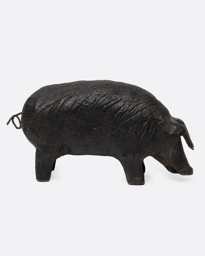 A wooden hand carved pig figurine with a wire tail, shown from the side.
