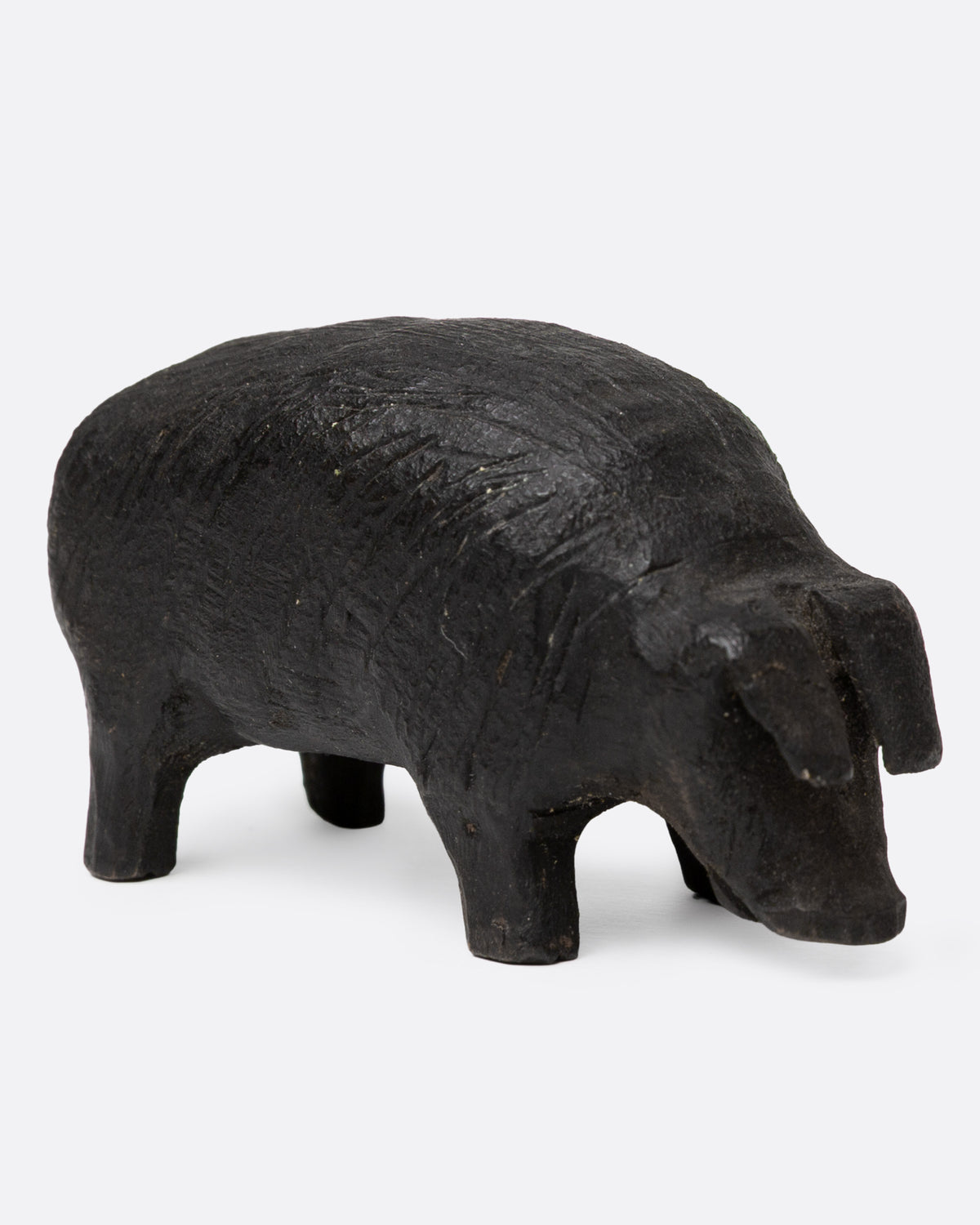 A wooden hand carved pig figurine with a wire tail, shown from the side.