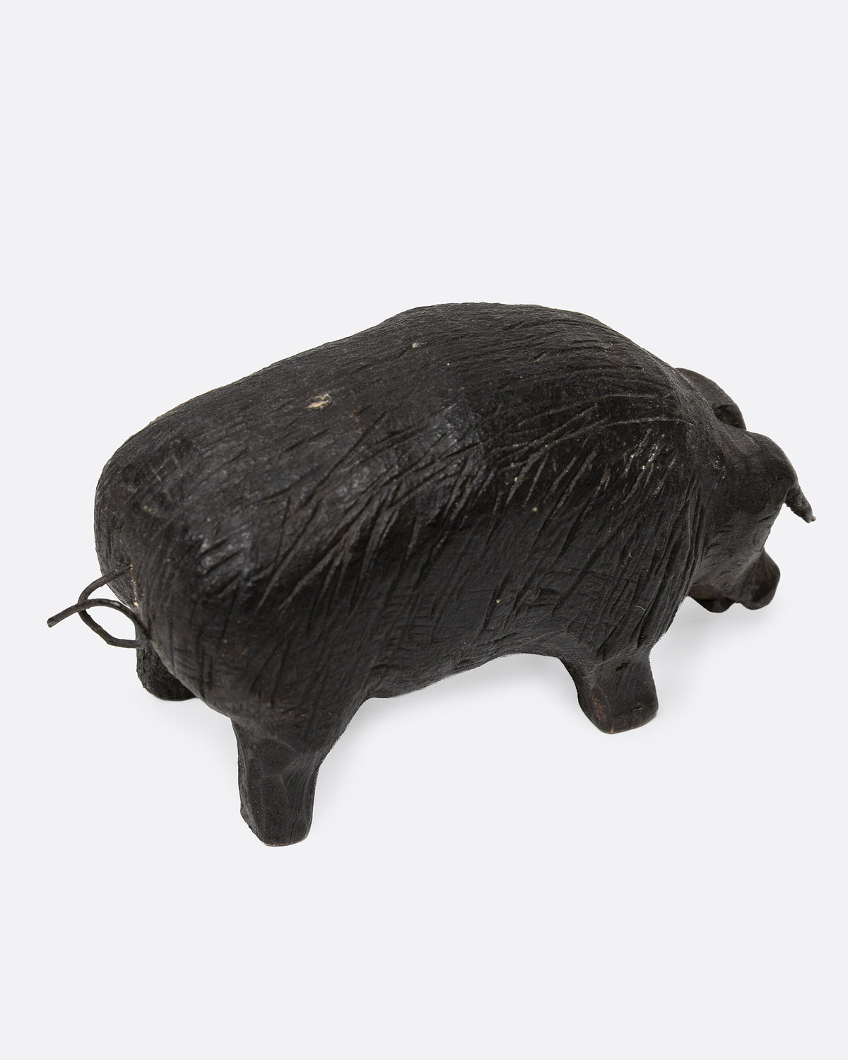 A wooden hand carved pig figurine with a wire tail, shown from the back.