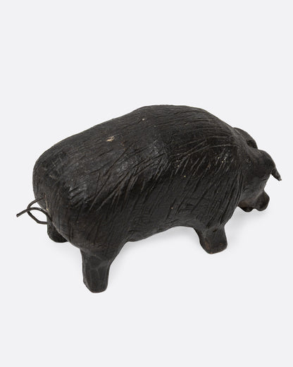A wooden hand carved pig figurine with a wire tail, shown from the back.