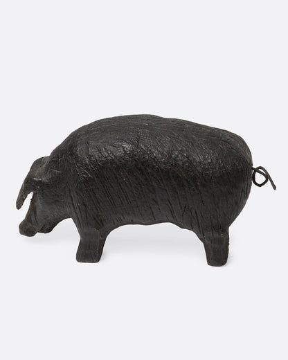 A wooden hand carved pig figurine with a wire tail, shown from the side.