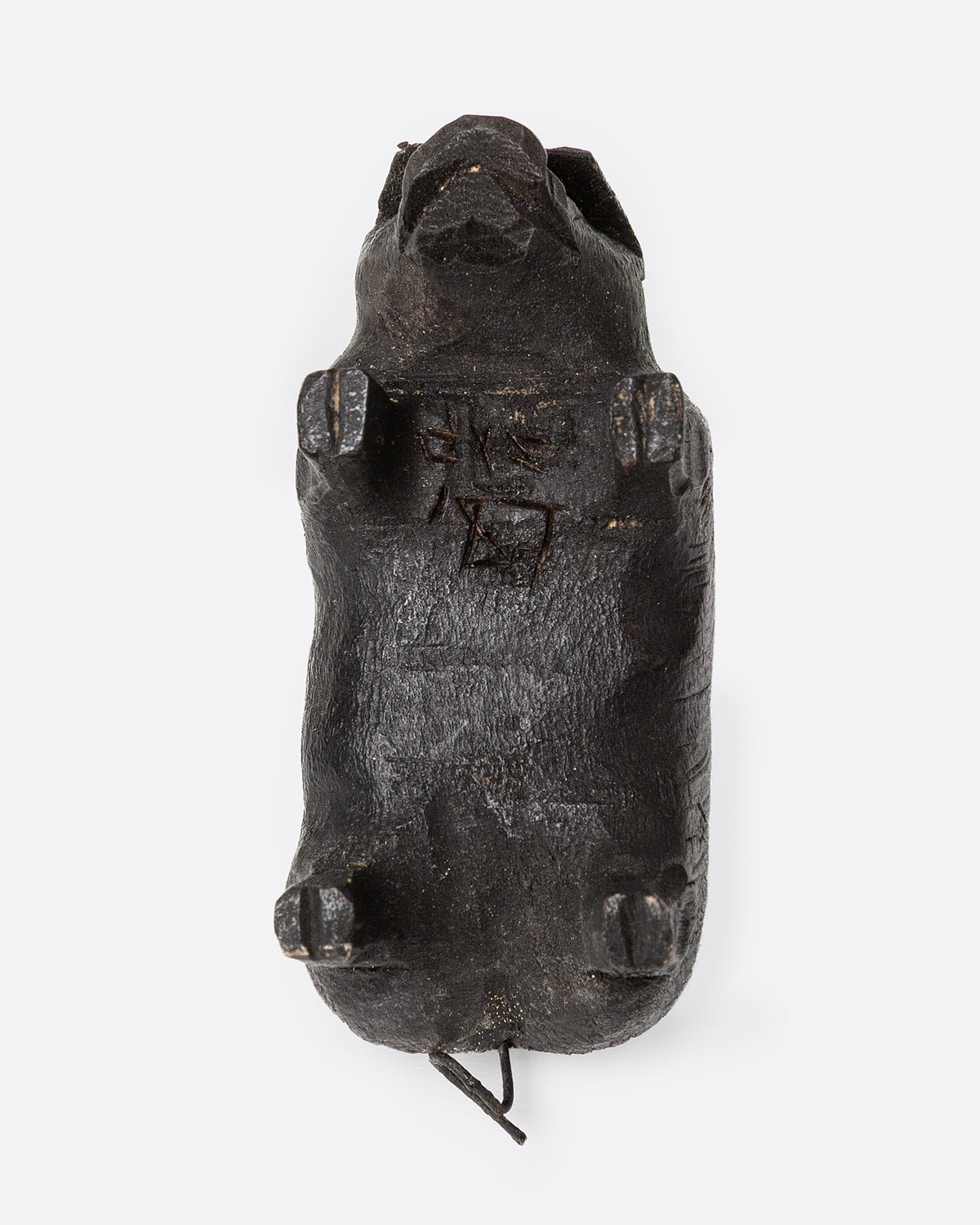 A wooden hand carved pig figurine with a wire tail, shown from the bottom.