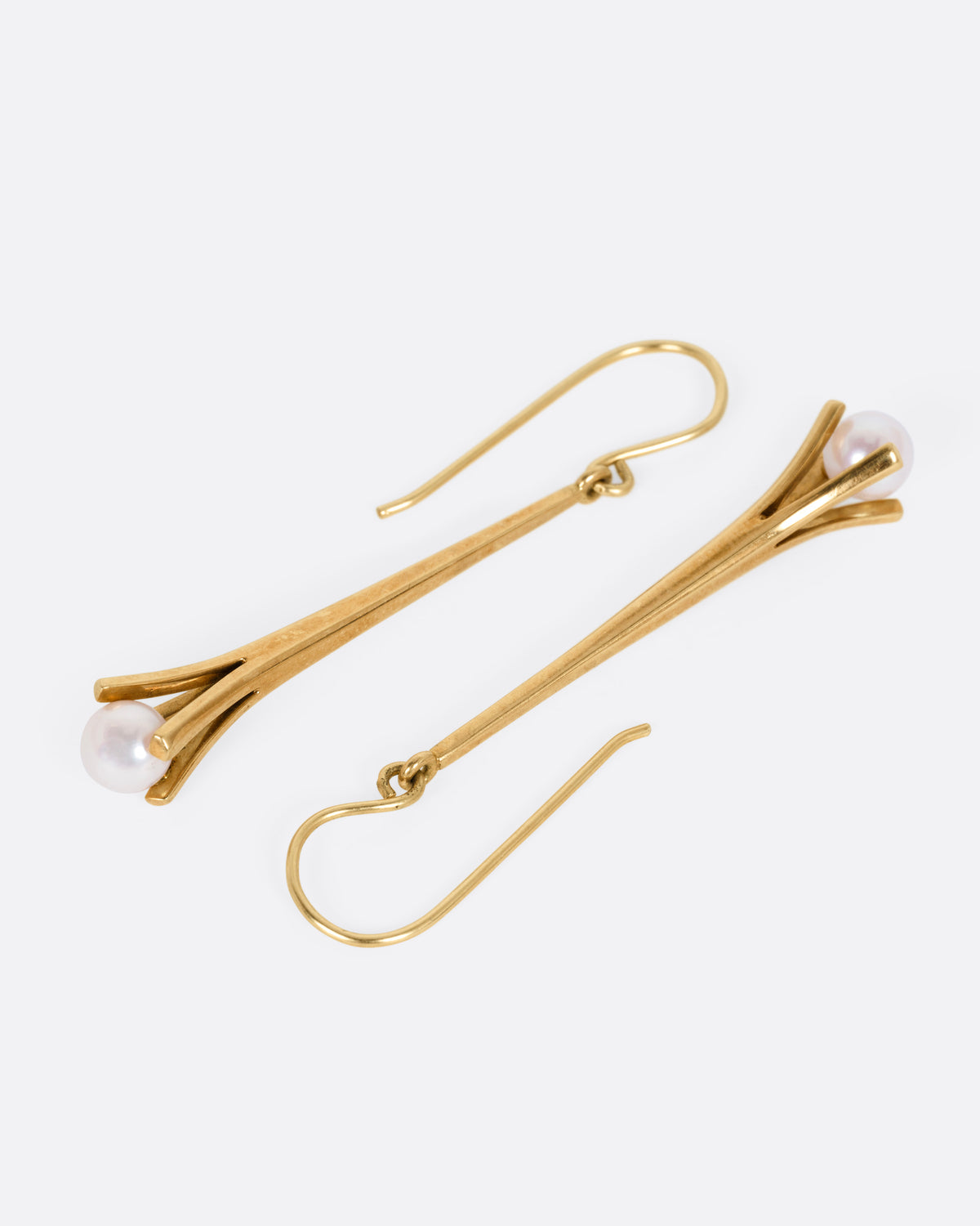 A pair of yellow gold drop earrings with a split vertical bar, and a single white pearl hanging from the bottom, shown from the side.