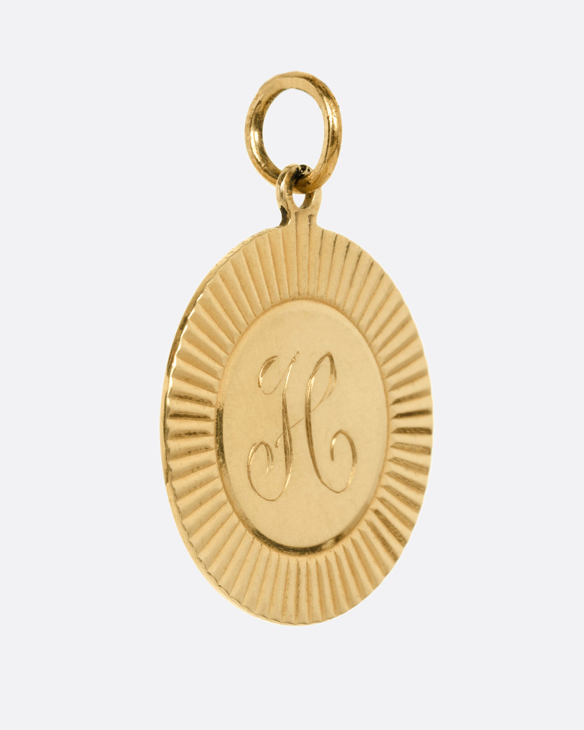 A round gold pendant with a sunburst radiating from a central engraved letter 'H', shown from the side.