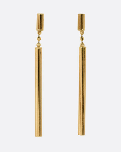 A pair of yellow gold drop earrings with a small cylindrical stud and a long, slender cylindrical dangle, shown from the front.