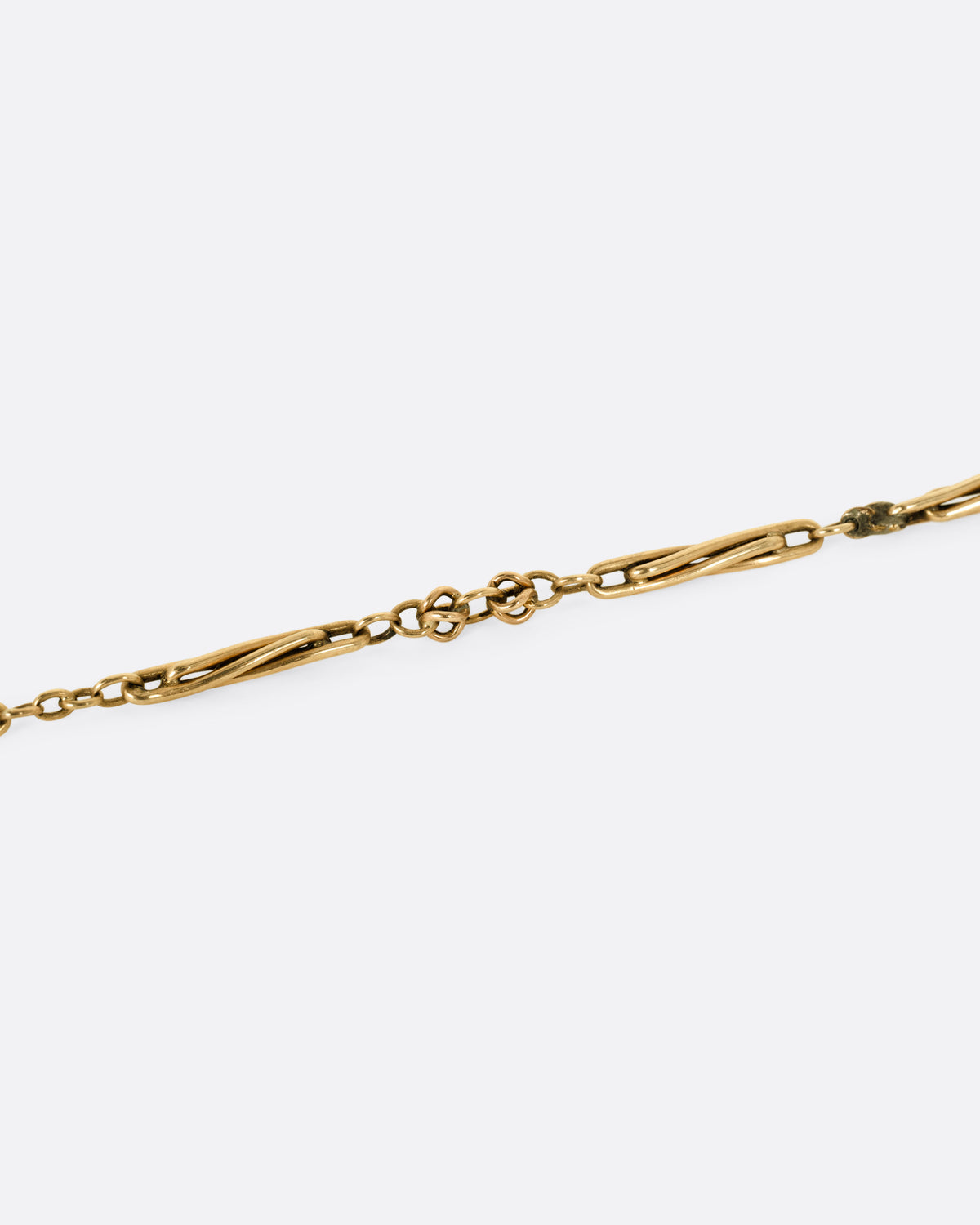 A close up of a yellow gold watch chain necklace with long twisted links.