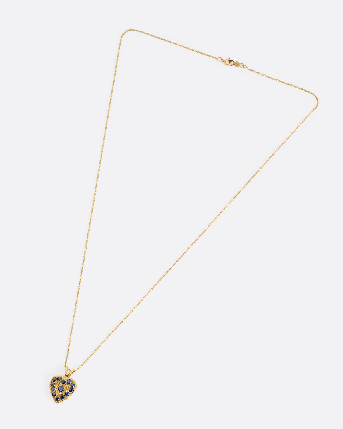 A yellow gold necklace with a heart shaped pendant with blue sapphires, shown from the front.
