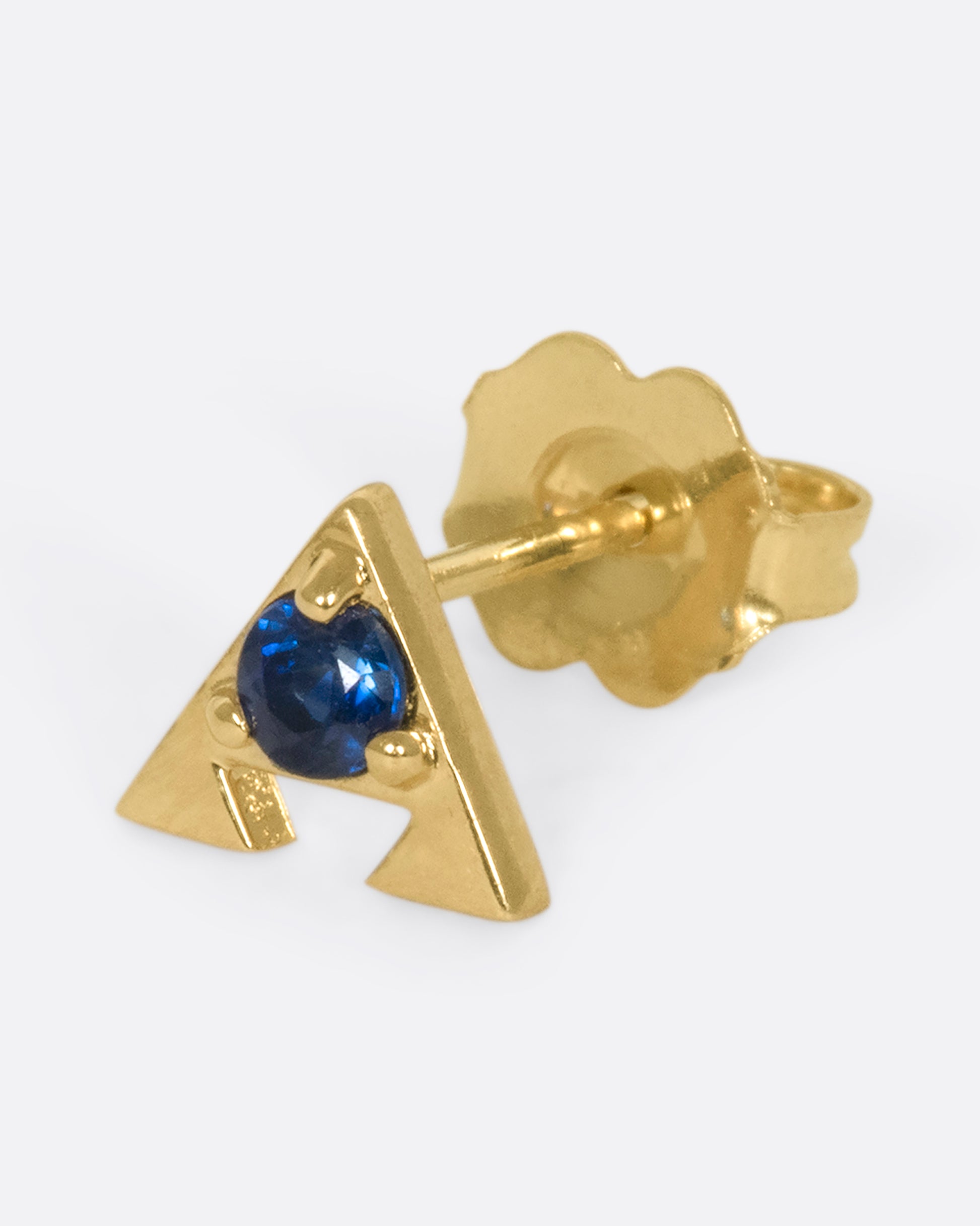 A 14k gold amulet stud with a blue sapphire in the center