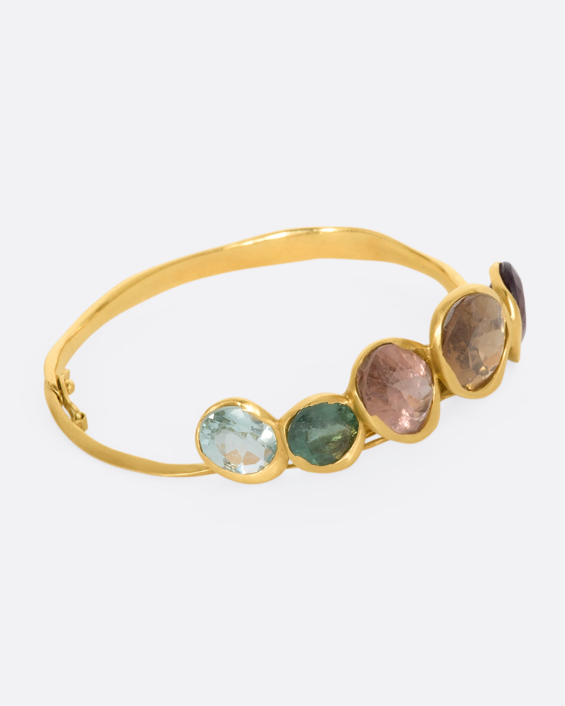 A yellow gold hinged bracelet crowned with five large different color tourmalines. View from the side.