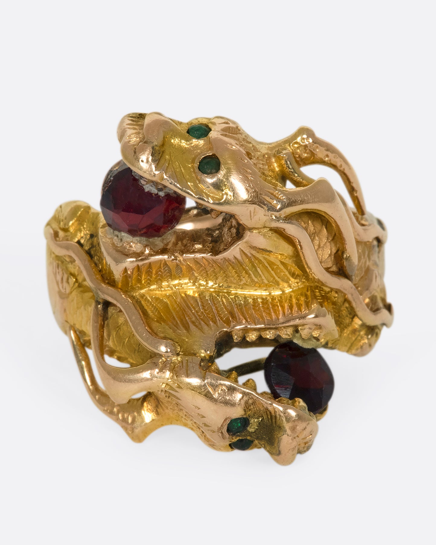A close up view of a yellow gold ring with two wrapped dragons, each with emerald eyes and garnets in their mouths.
