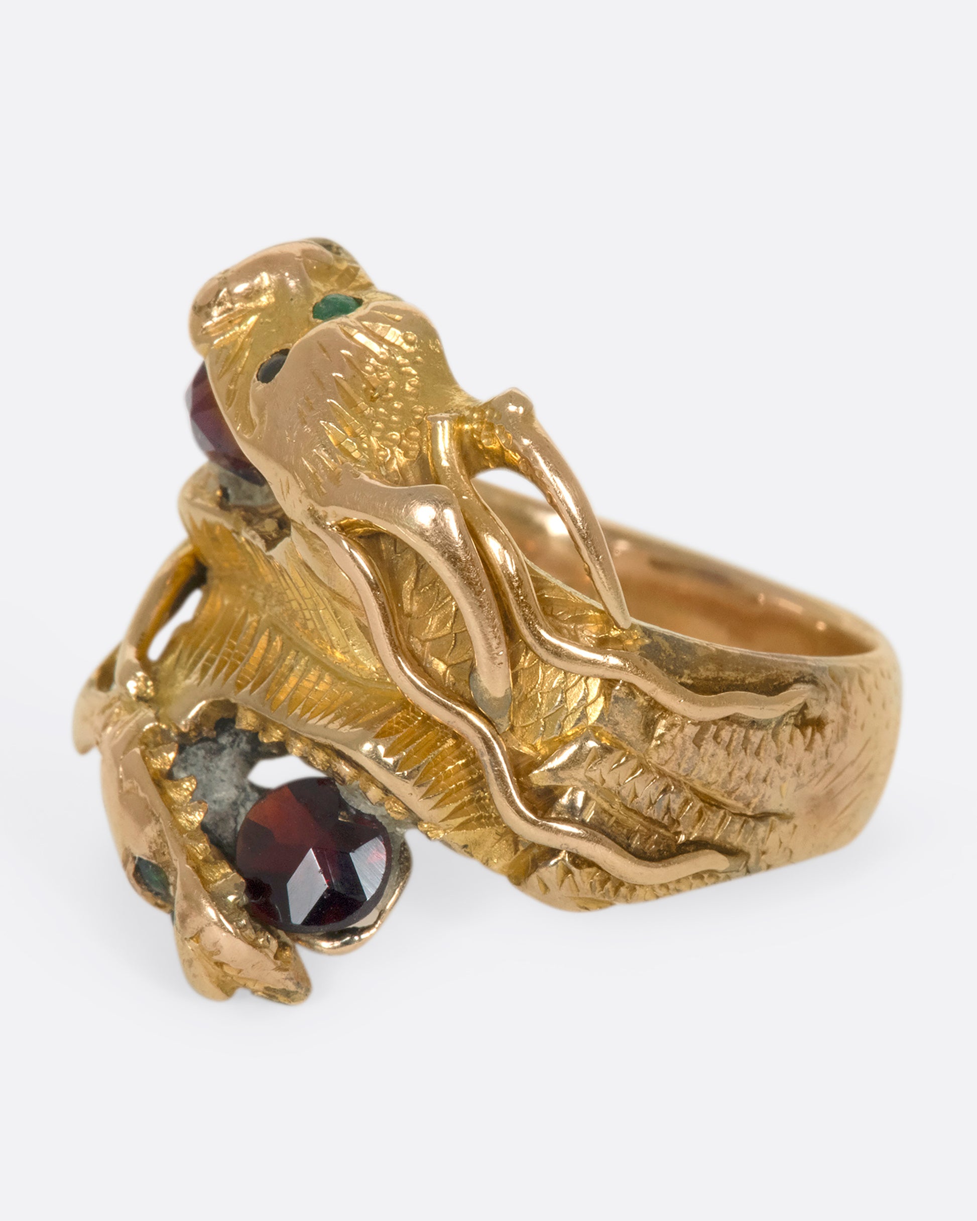 A left side view of a yellow gold ring with two wrapped dragons, each with emerald eyes and garnets in their mouths.