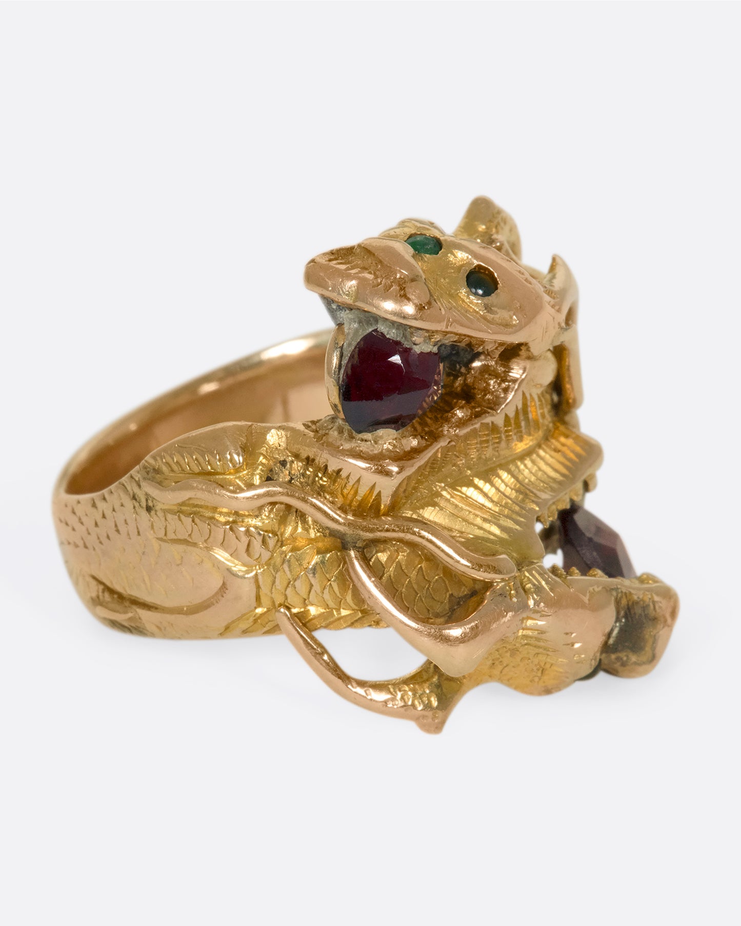 A right side view of a yellow gold ring with two wrapped dragons, each with emerald eyes and garnets in their mouths.