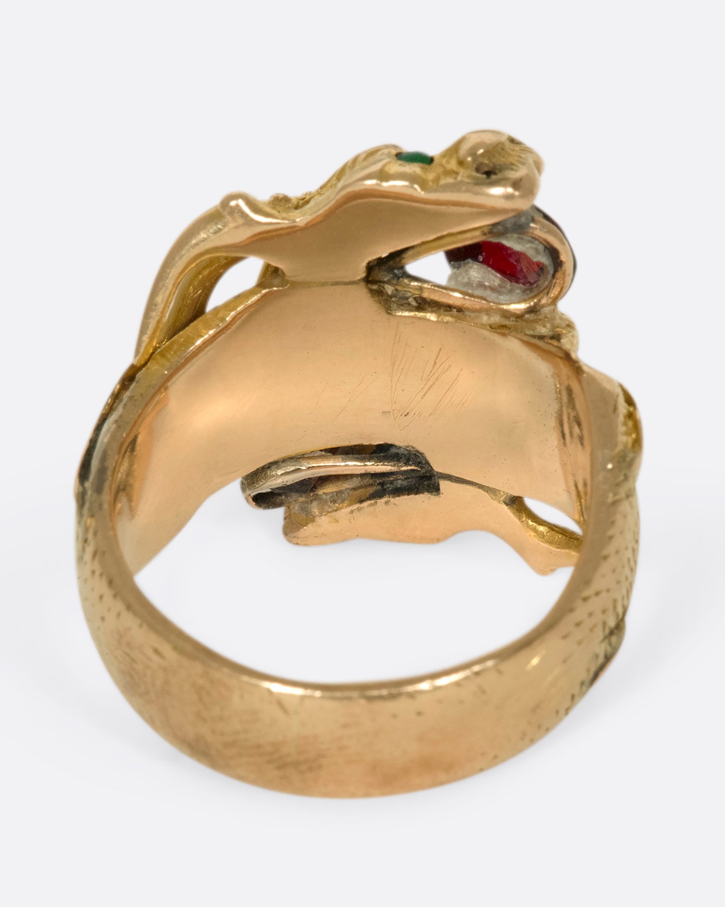 A view of the underside of a yellow gold ring with two wrapped dragons, each with emerald eyes and garnets in their mouths.