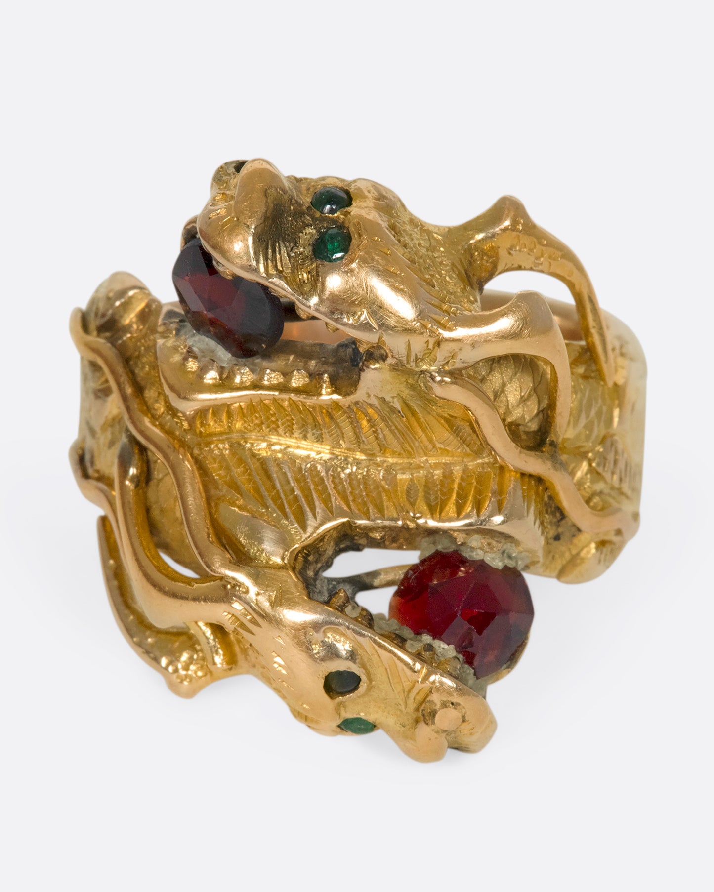 A slightly off center view of a yellow gold ring with two wrapped dragons, each with emerald eyes and garnets in their mouths.