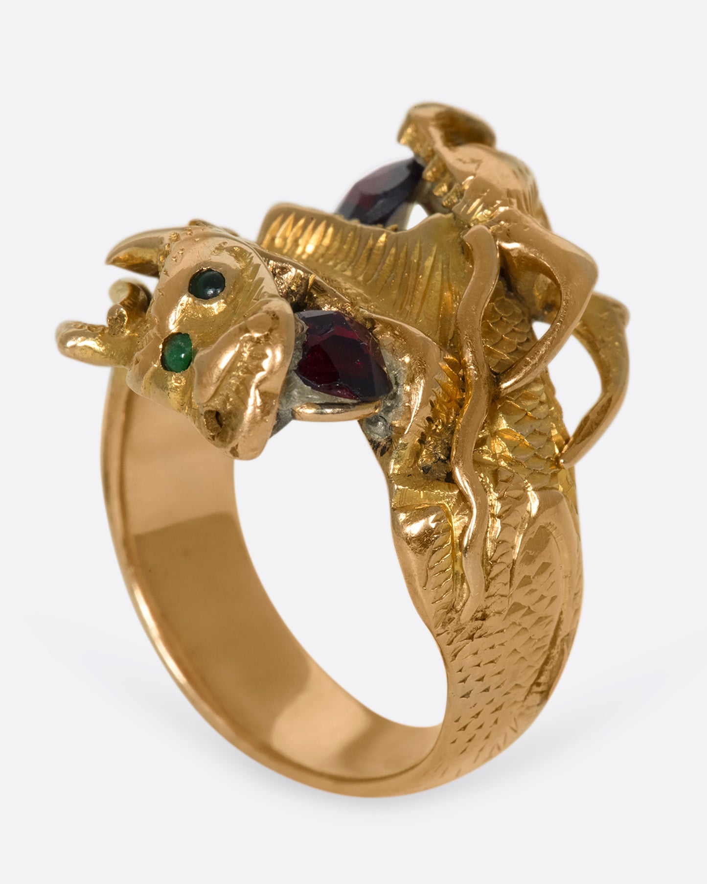 A view of a yellow gold ring with two wrapped dragons, each with emerald eyes and garnets in their mouths standing on its band.