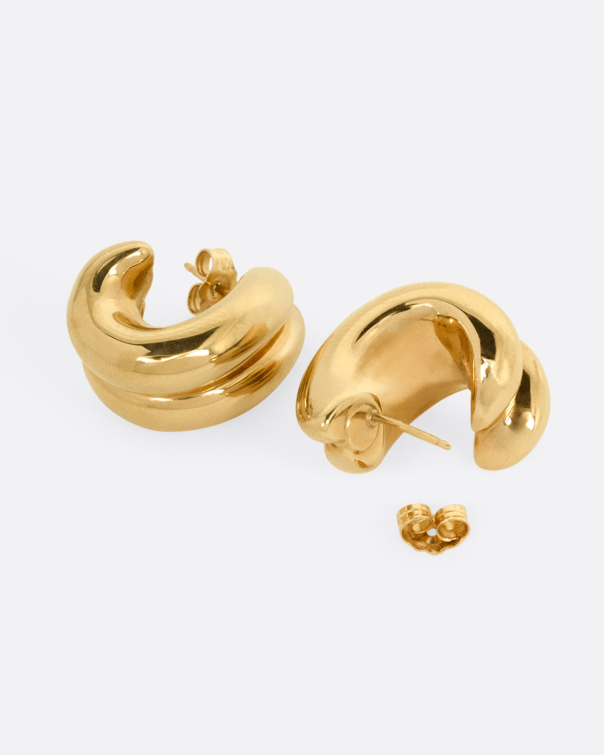 A pair of yellow gold curved huggie earrings, shown from the side with one earring open.