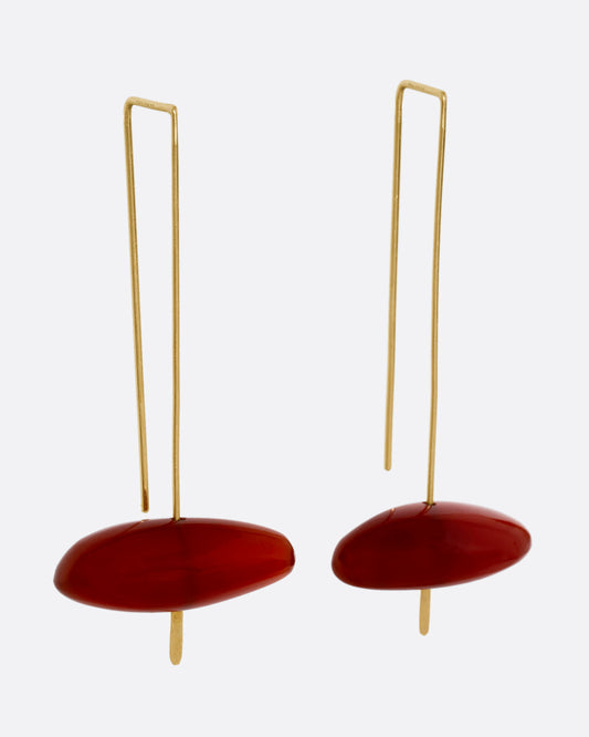 A pair of long yellow gold earrings with freeform carnelians at each base, shown from the side.