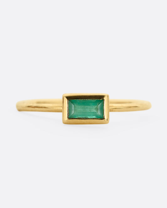 A yellow gold ring with an emerald baguette, shown from the front.