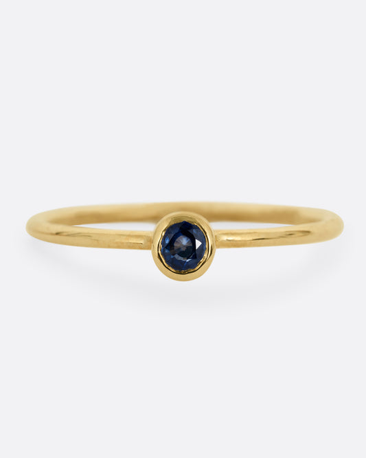 A yellow gold ring with a round sapphire, shown from the front.
