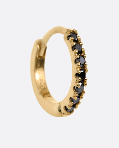 A yellow gold hinged hoop earring with black pavé diamonds, shown from the side.