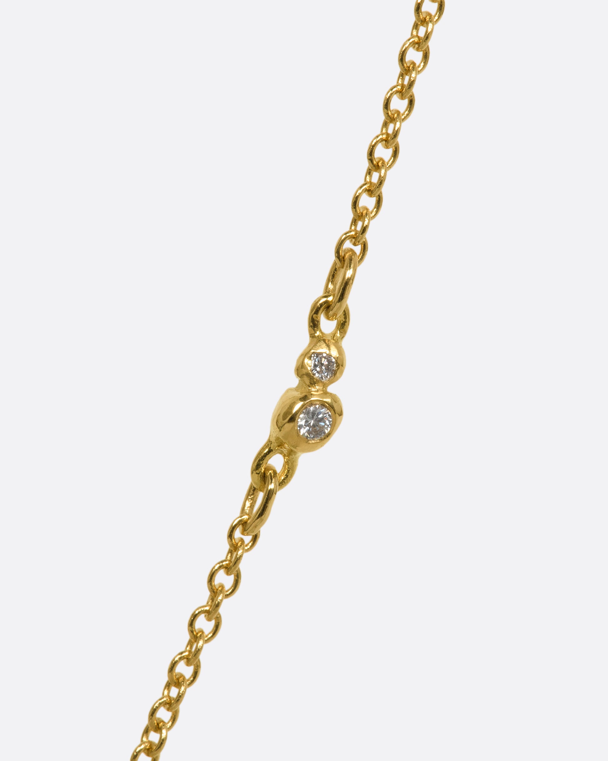 A yellow gold necklace with a rose cut solitaire diamond pendant and a cluster  of diamonds on the chain. View of the two diamond cluster.