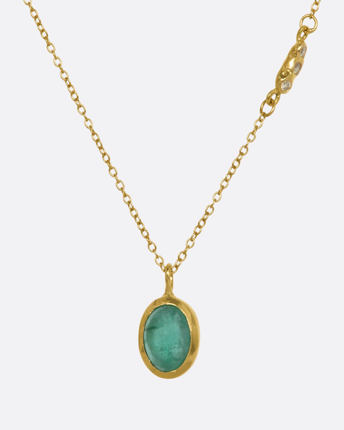 A yellow gold necklace with an oval cabochon emerald pendant and triple diamond cluster spacer. View from the front.