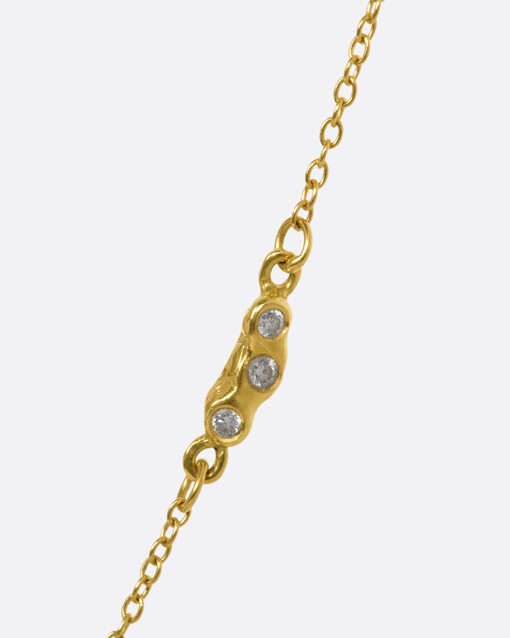 A yellow gold necklace with an oval cabochon emerald pendant and triple diamond cluster spacer. View of the diamond cluster spacer.