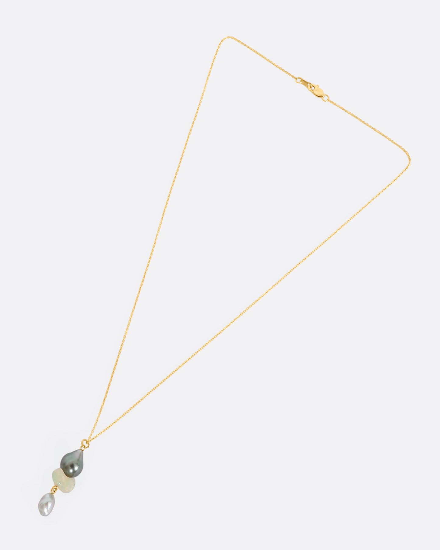 A yellow gold necklace with a triple drop pendant consisting of one opal and two pearls. View laying flat.