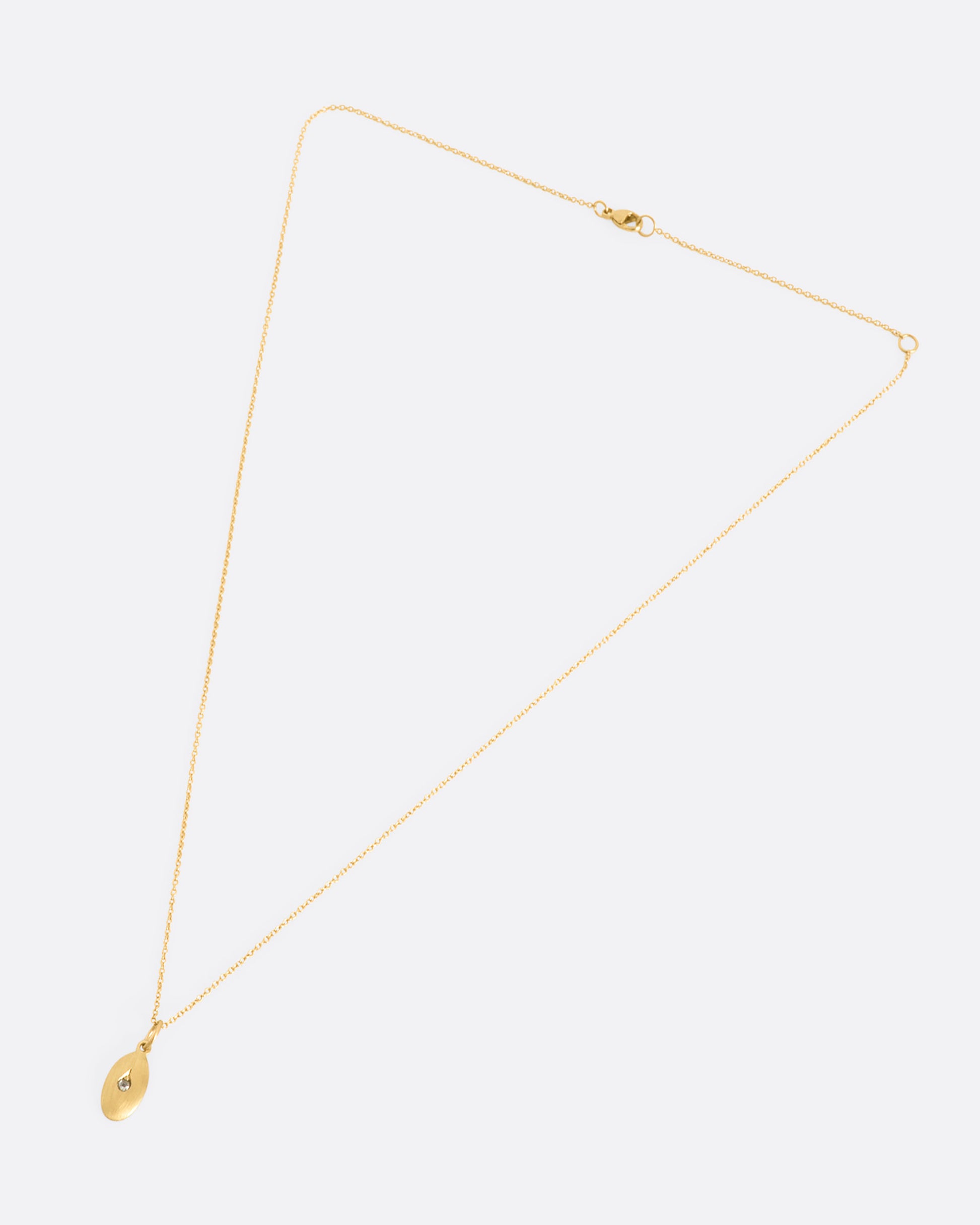 A yellow gold oval pendant with a diamond at the center. View of the full necklace, laying flat.