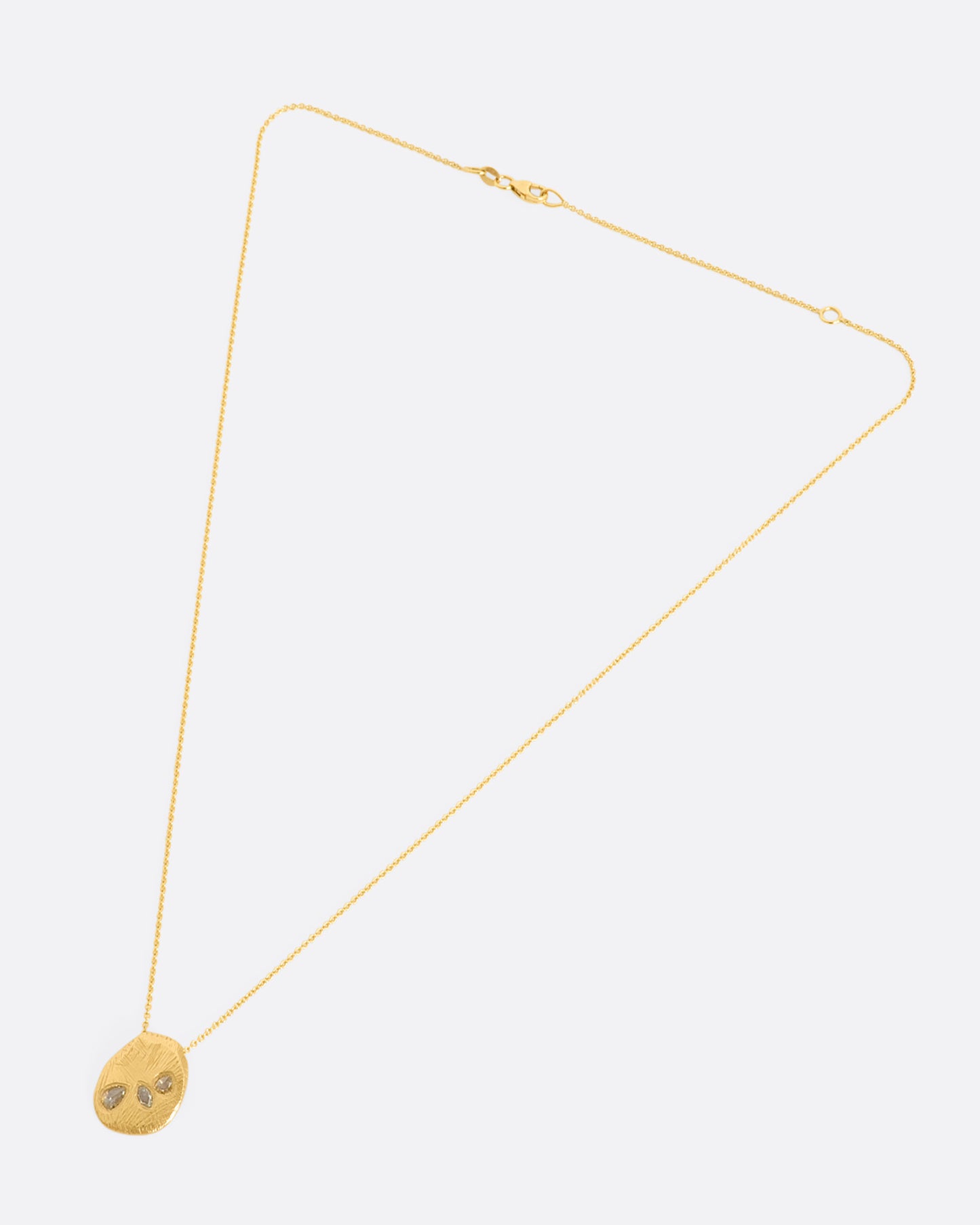 A heavy, hand carved, sliding gold pendant with three rose cut diamonds on a cable chain. View laying flat.