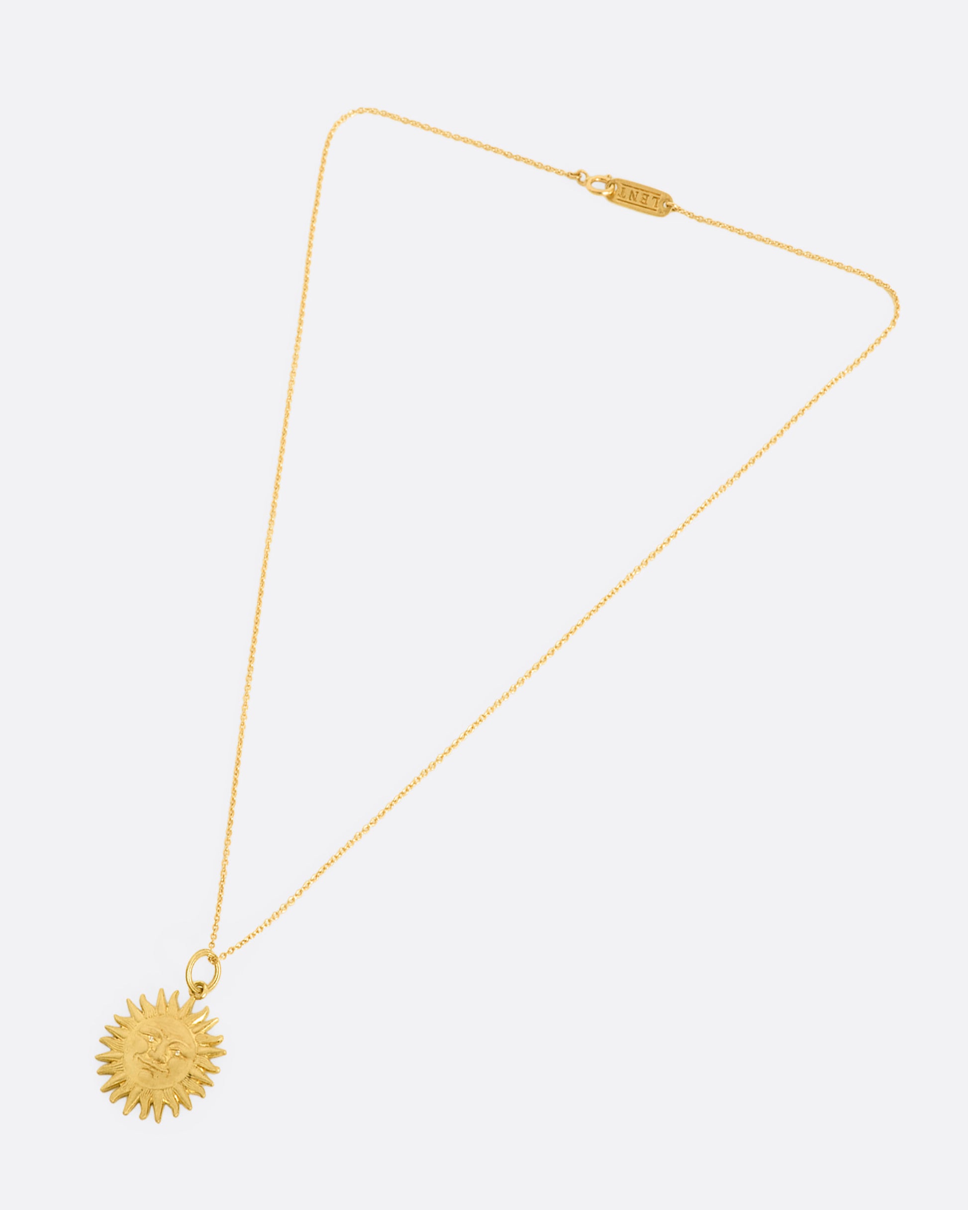 Yellow gold sun pendant with diamond eyes, view laying flat.