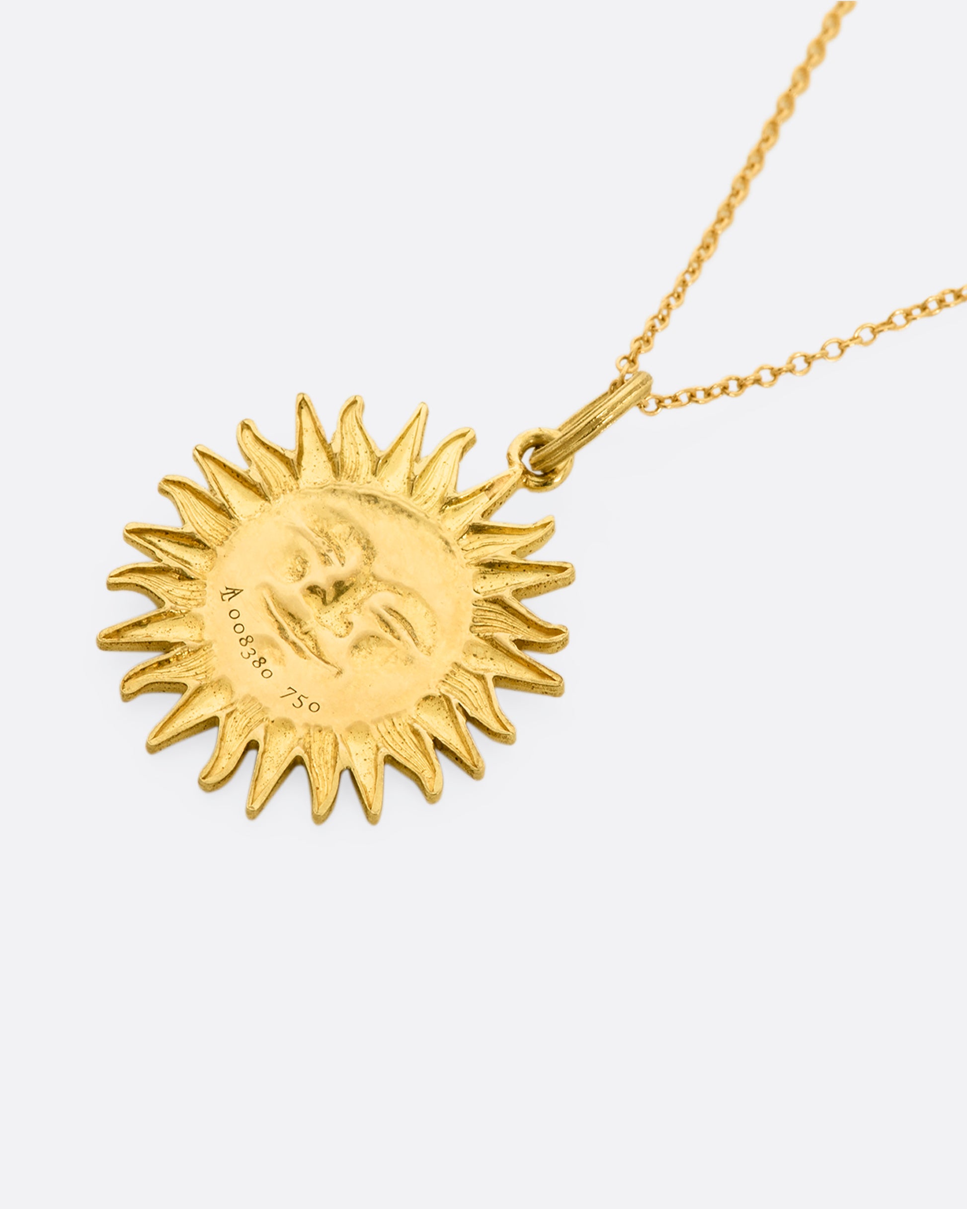 Yellow gold sun pendant with diamond eyes, view laying flat of the back.