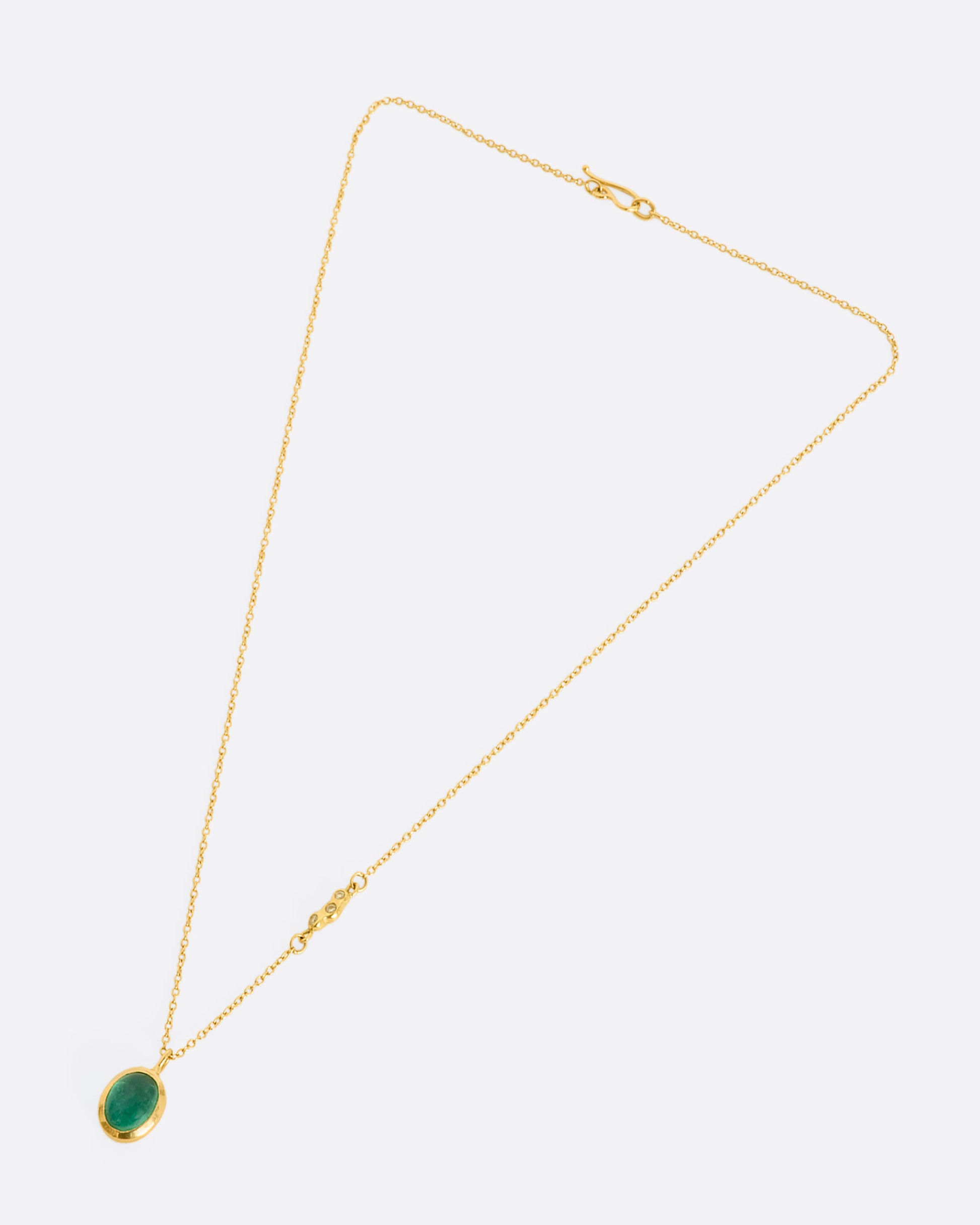 A yellow gold necklace with an oval cabochon emerald pendant and triple diamond cluster spacer. View laying flat.