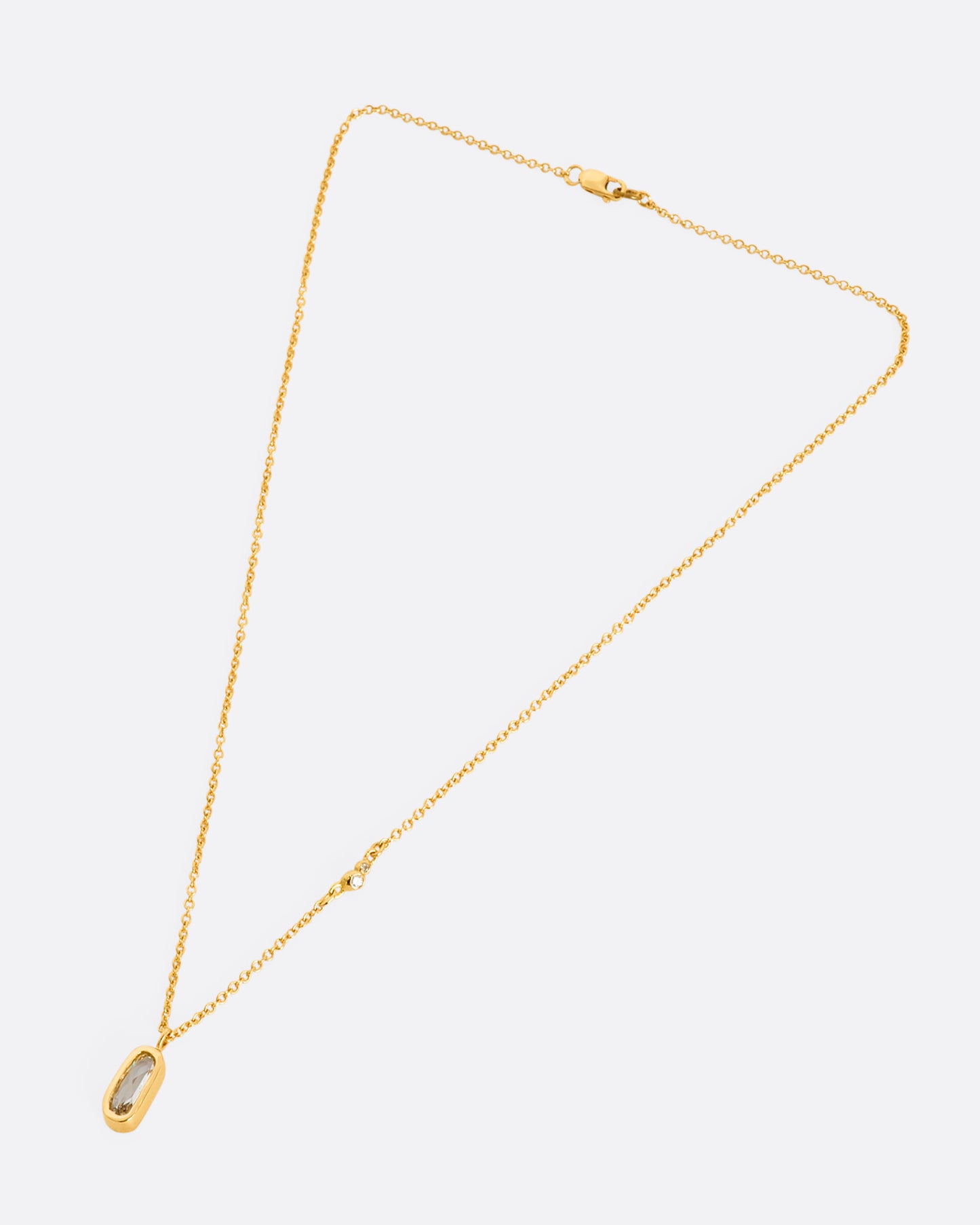 A yellow gold necklace with a rose cut solitaire diamond pendant and a cluster  of diamonds on the chain. View of the entire necklace, laying flat from above.