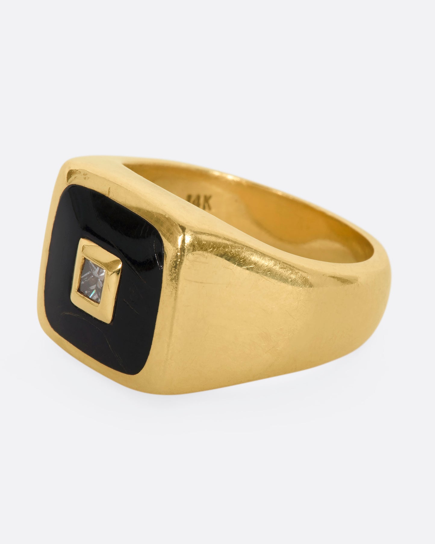 A yellow gold signet ring with onyx inlay and a princess cut diamond. View from the side.