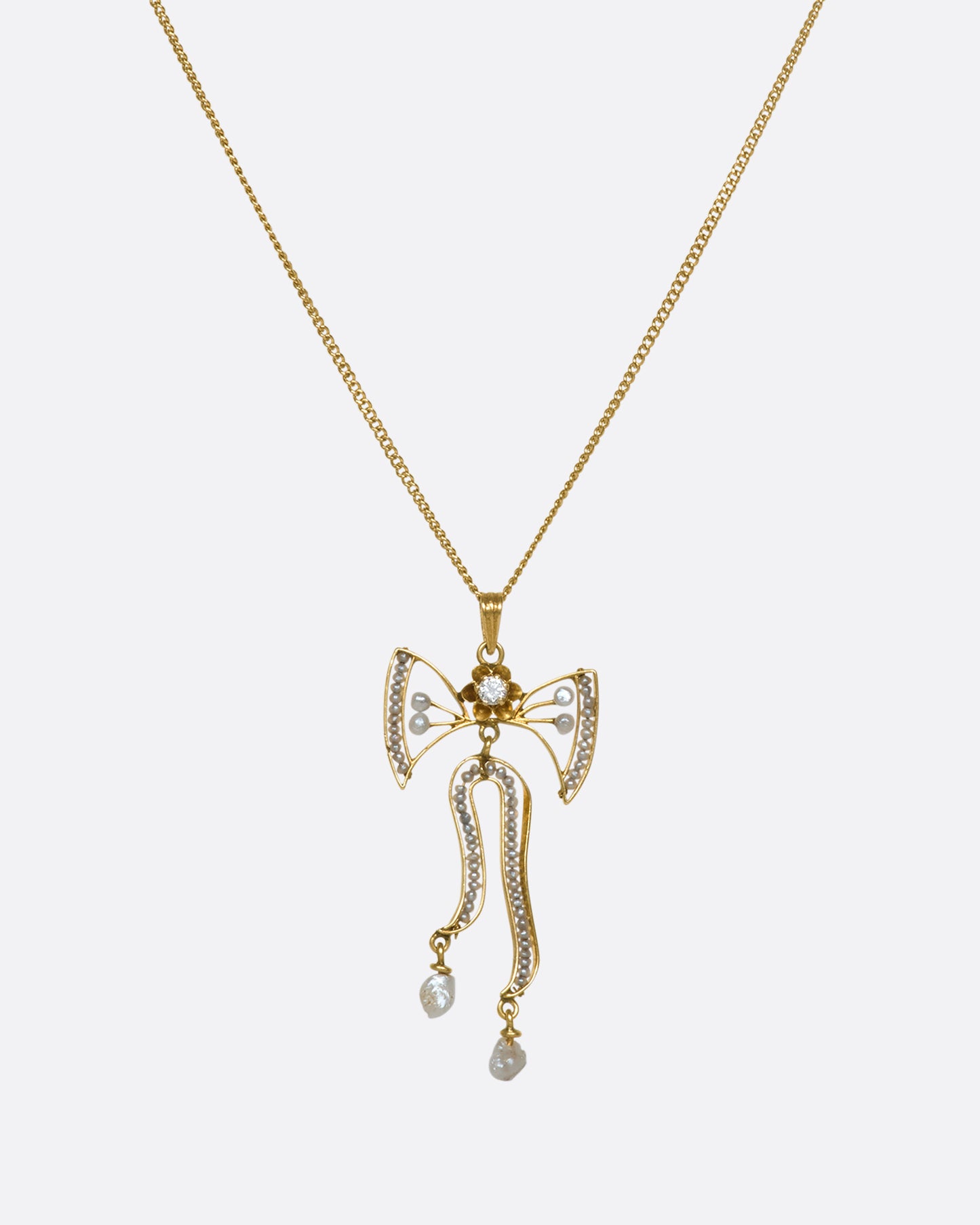 A pulled out view of a hanging yellow gold bow pendant with seed pearls and a diamond with the majority of the chain showing.