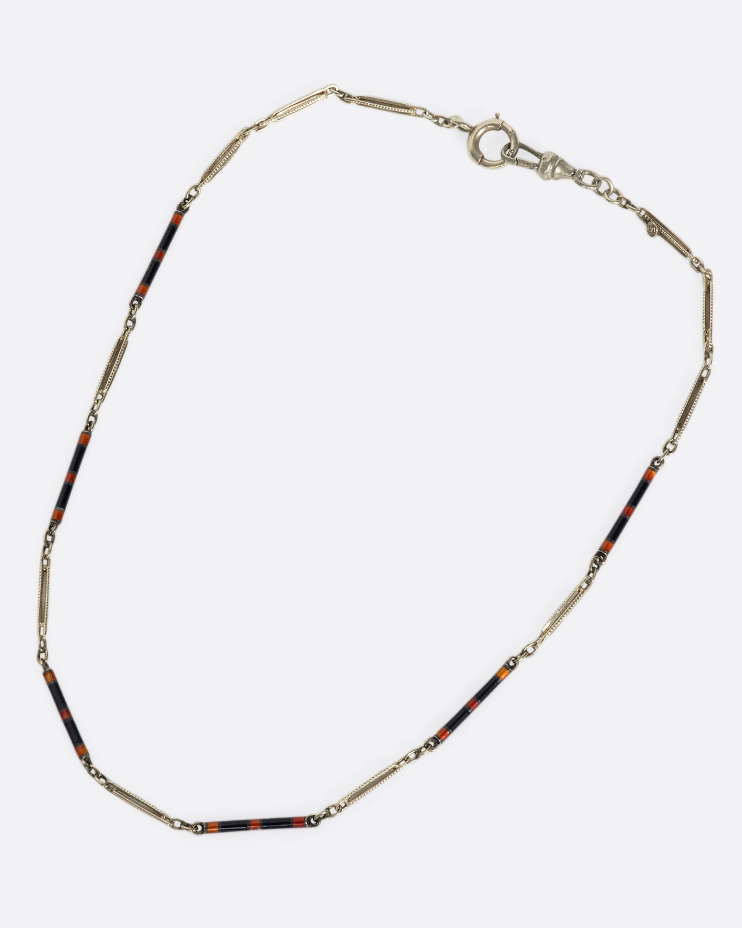 An overhead view of a white gold chain necklace with black and red enamel sections laying down flat.