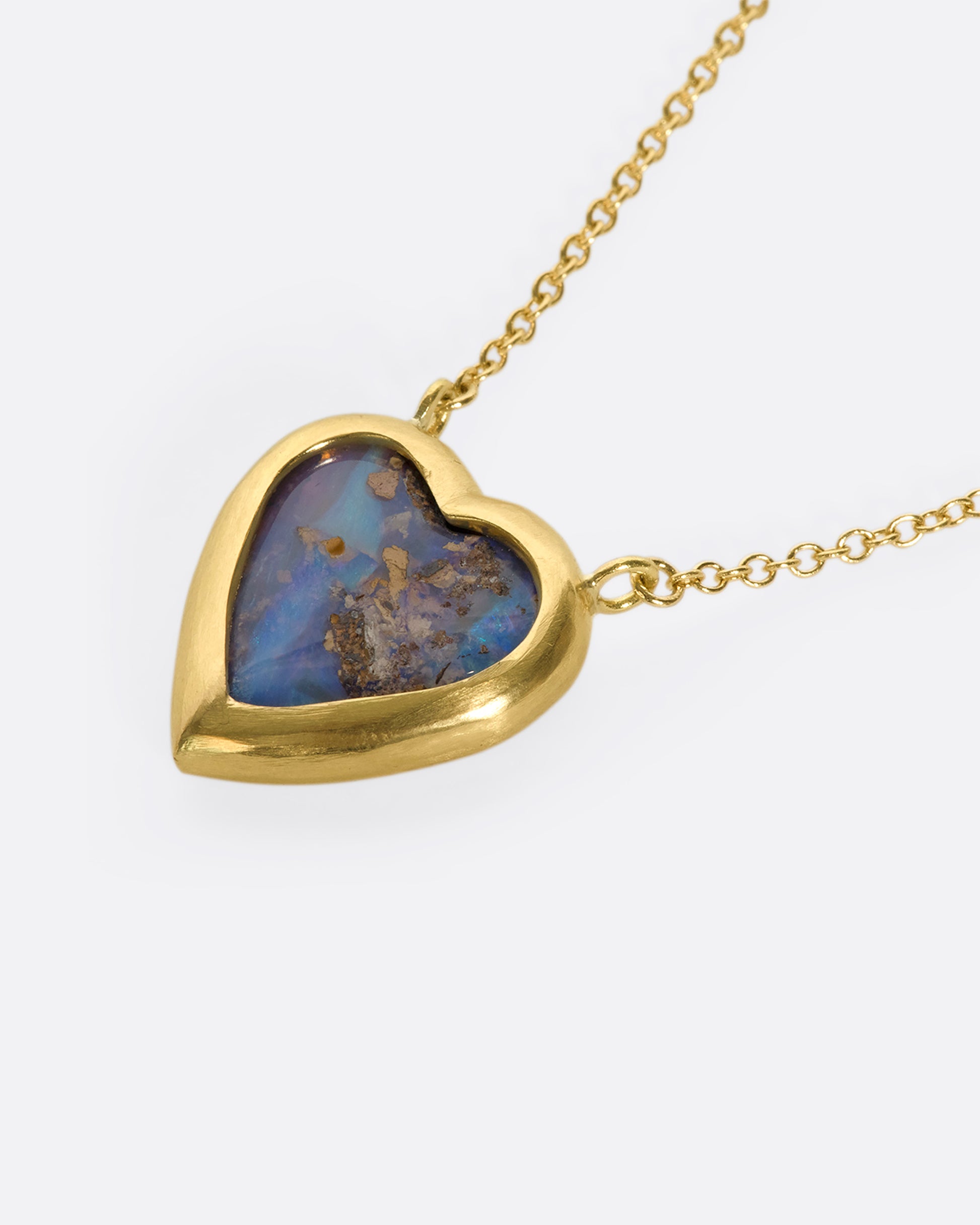 An opal heart pendant enwrapped with an 18k gold bezel setting, suspended on a fine gold chain with diamond spacers