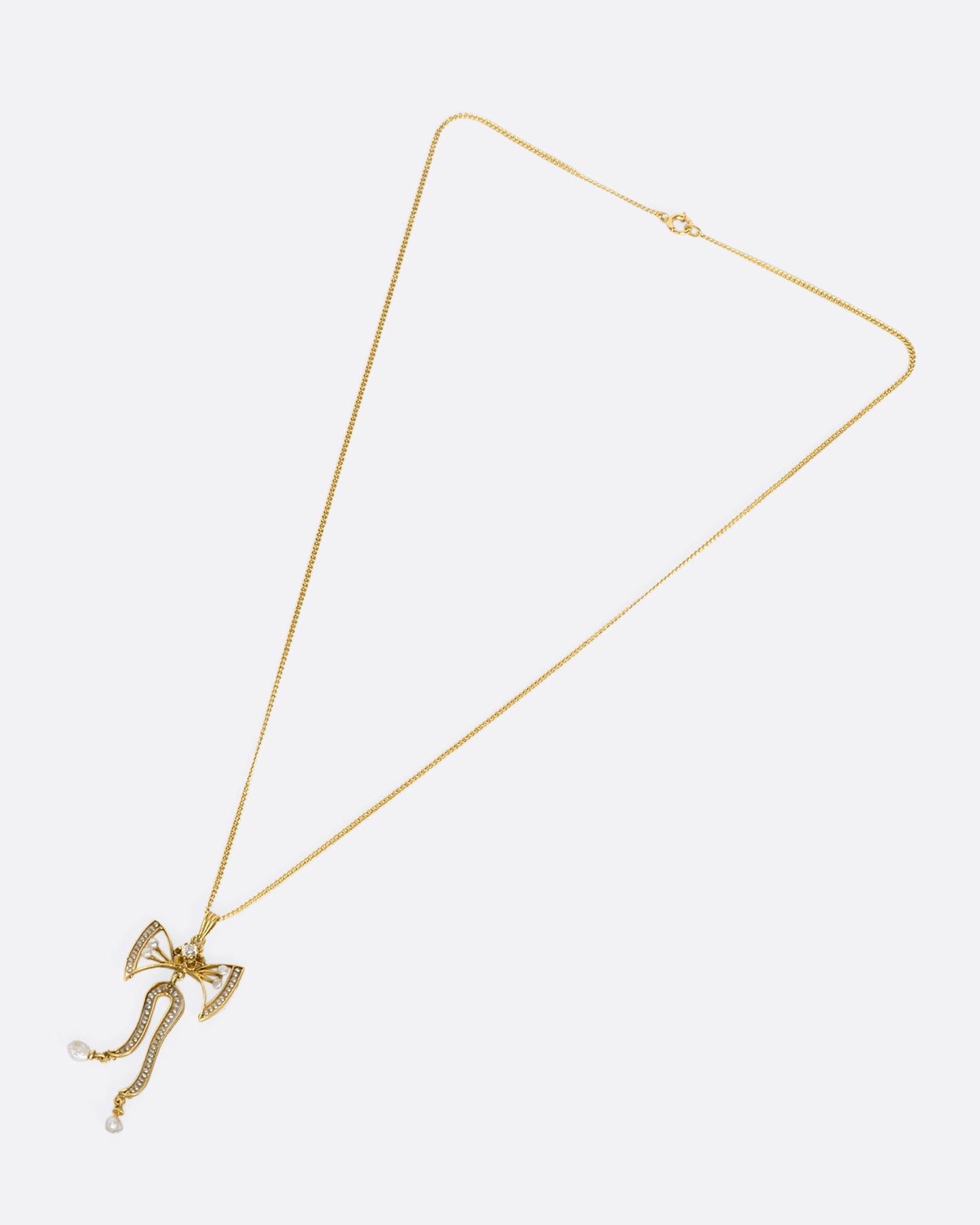 An overhead view of a yellow gold bow pendant with seed pearls and a diamond laying down flat with the chain pulled out in a triangular formation.