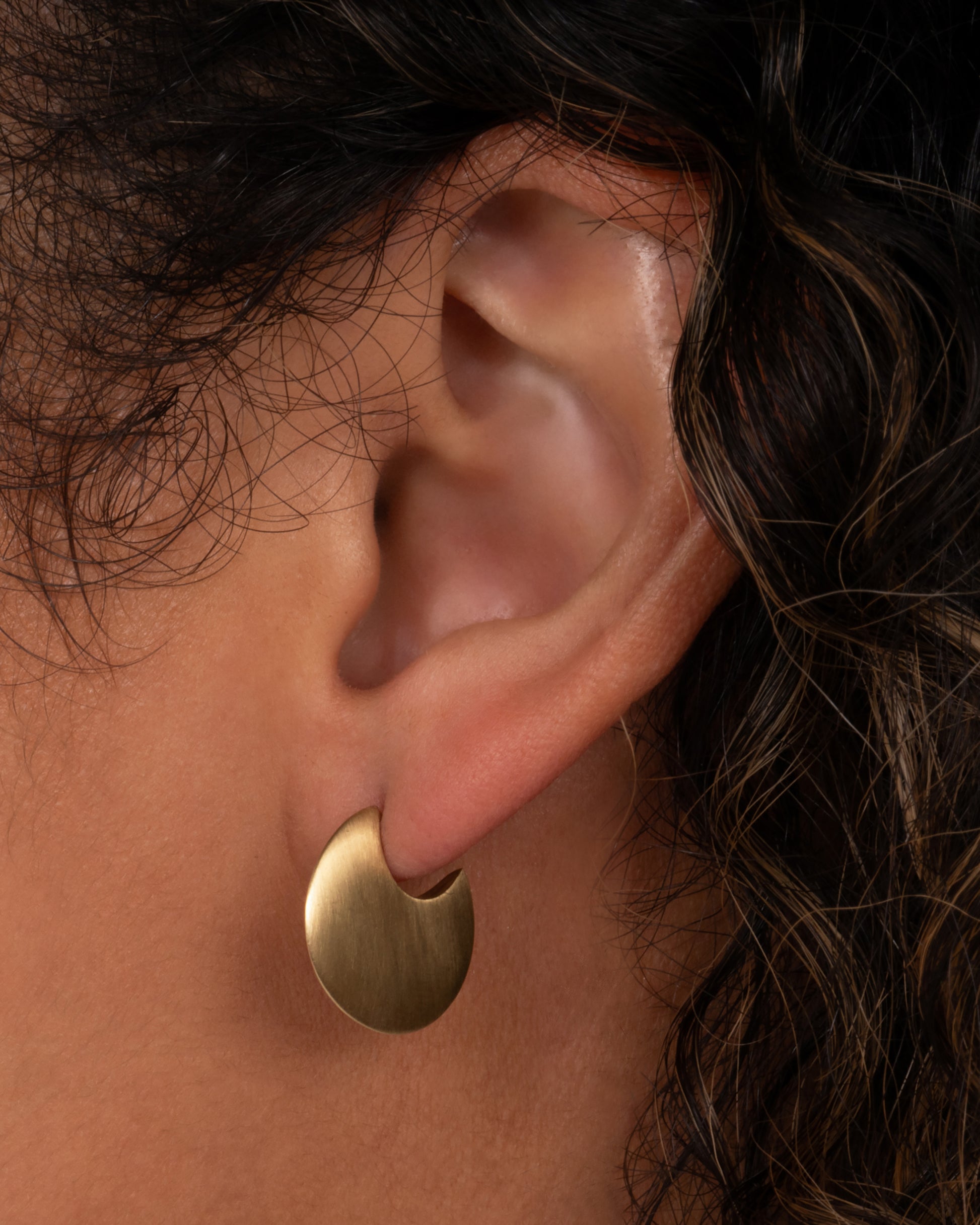 From the front, this pair of 10K solid gold hoop earrings look razor thin. Shown worn in an ear.