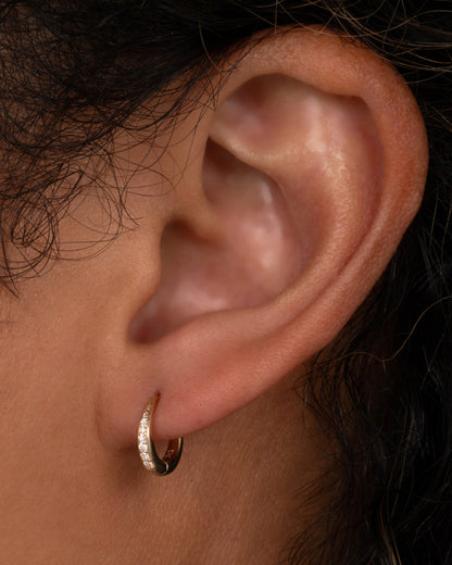 A yellow gold tapered hoop earring with a queue of graduated diamonds, shown on a person.