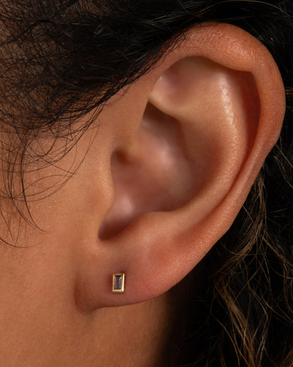 A yellow gold stud earring with a baguette cut tanzanite. Shown in an ear.