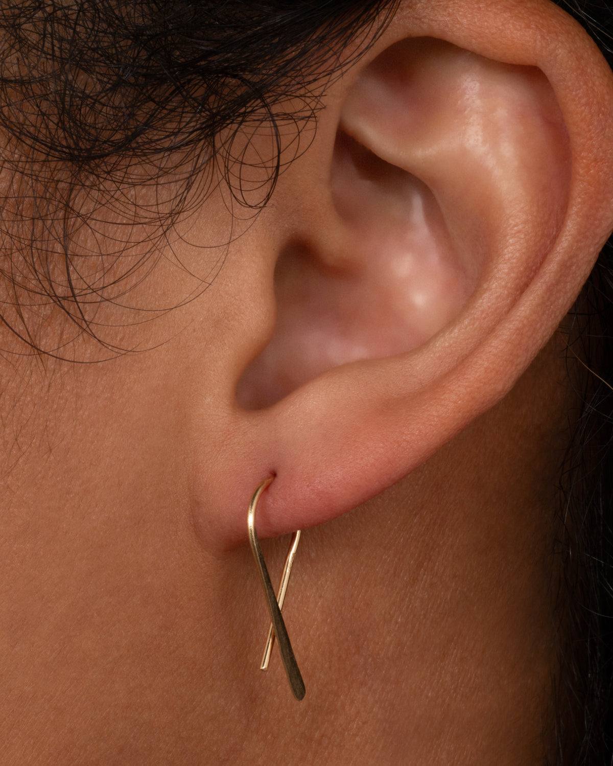 Christine Fail medium crossed hook earring in Fairmined gold worn on an ear, a thin wire looped so the ends cross