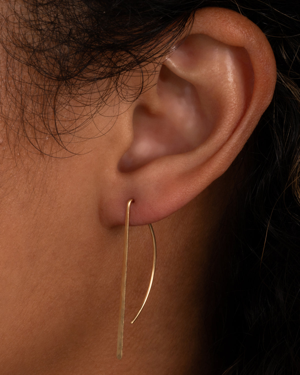 Christine Fail medium bow hook earring in Fairmined gold worn on an ear, a thin wire bent into a half circle