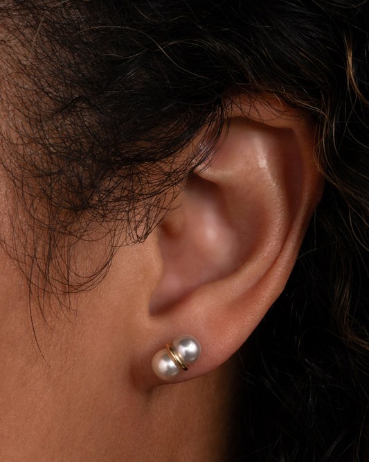 A pearl earring with a gold loop around the middle, shown worn in an ear.