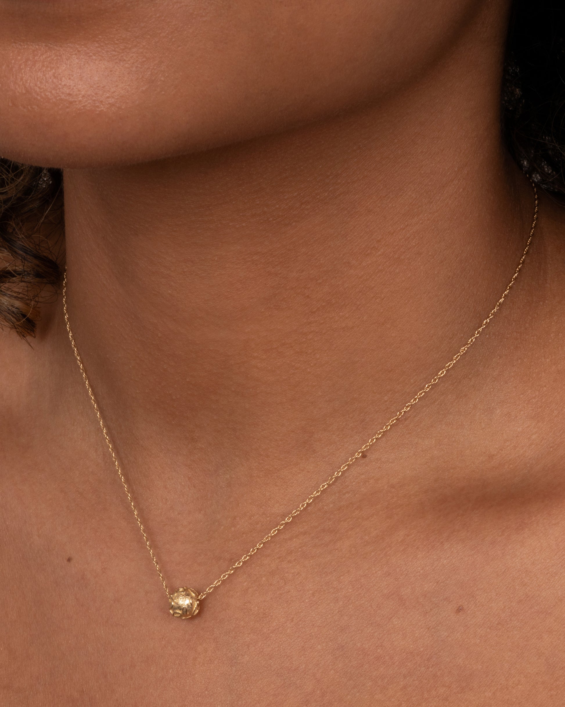 A yellow gold cable chain with a textured gold bead, shown worn around the neck.