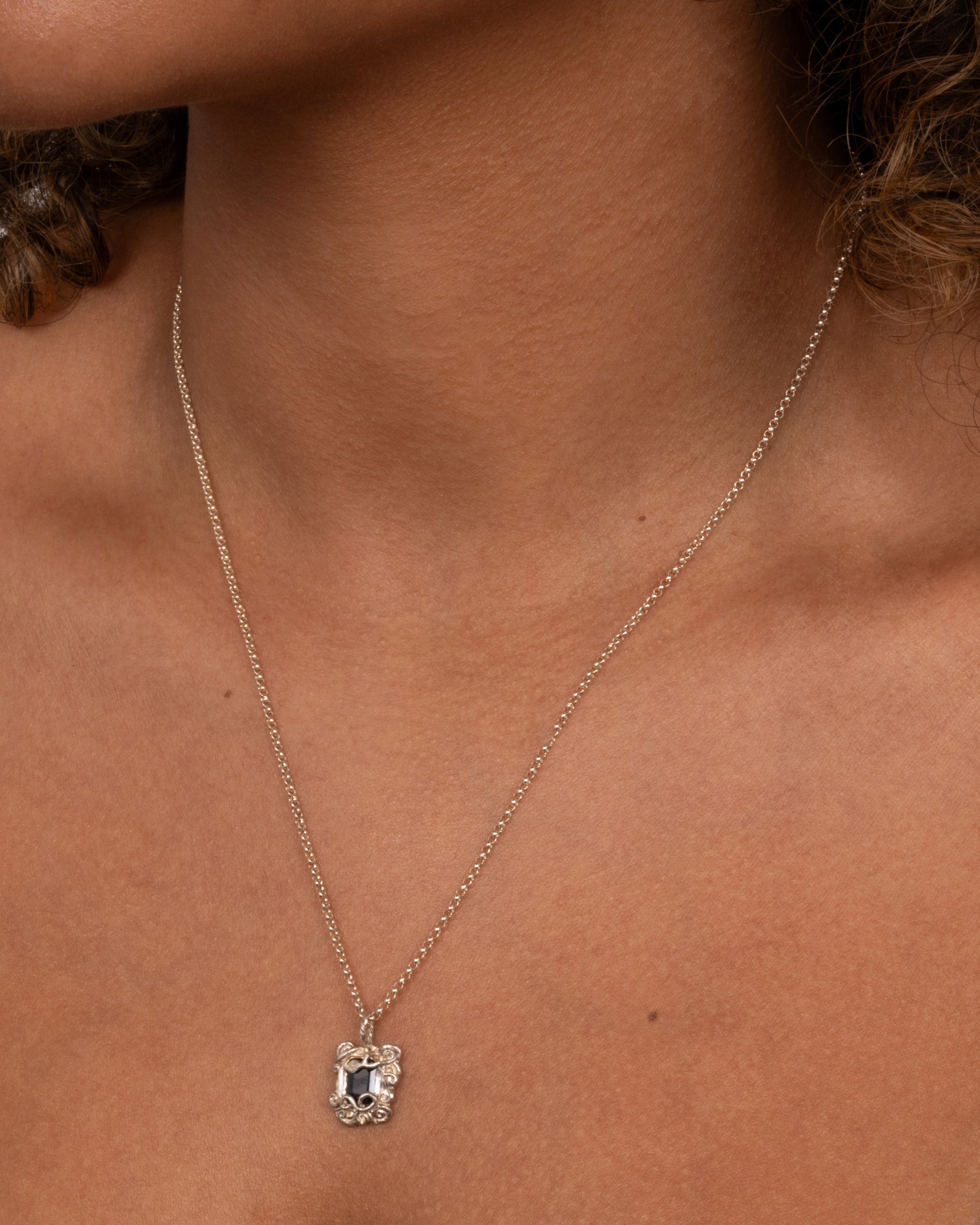 A silver pendant necklace with a deep blue sapphire in a setting with creeping vines. Shown worn around neck.
