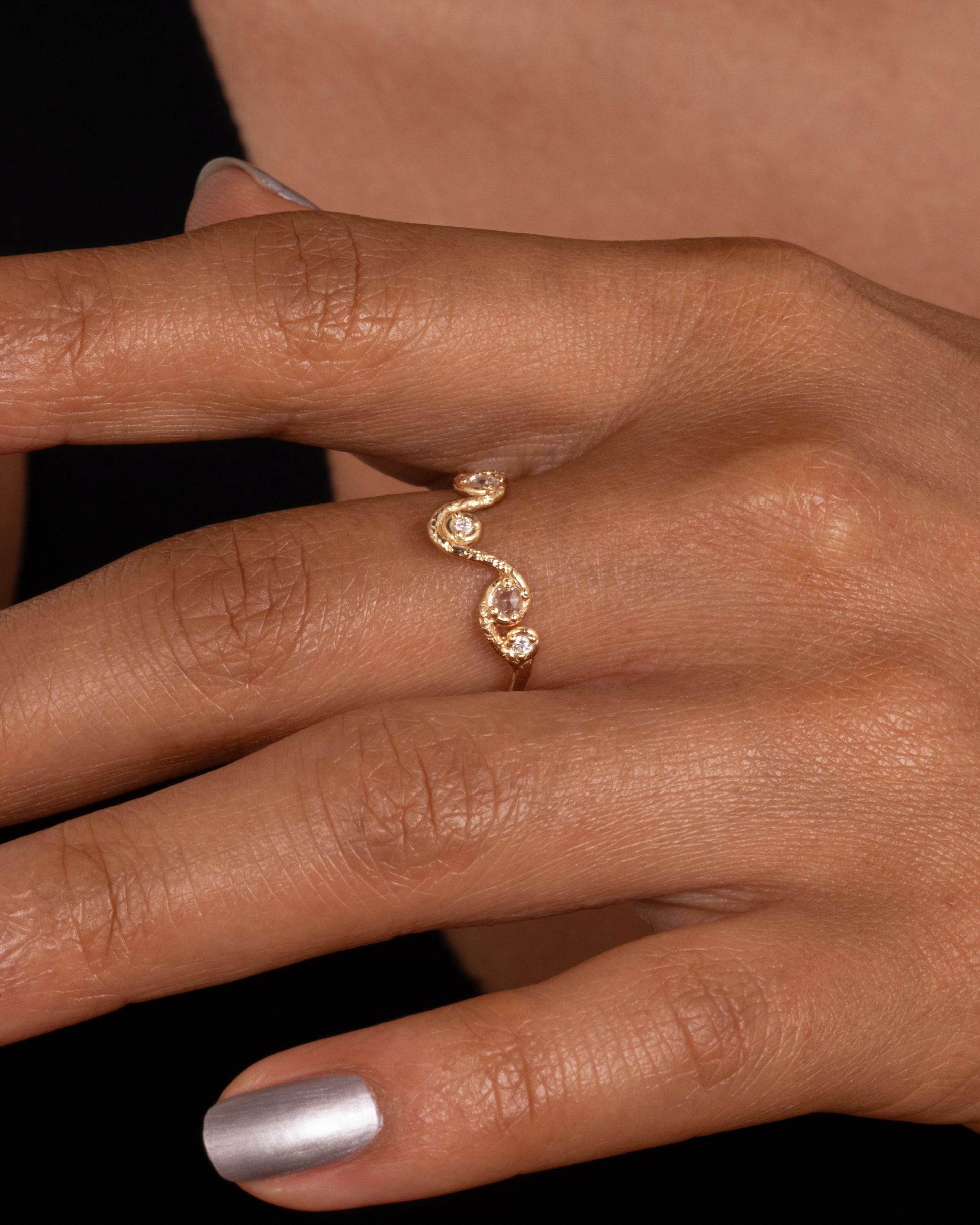 A wavy yellow gold ring with five round diamonds. Shown worn on finger.